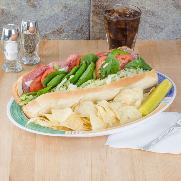 A Diamond Barcelona oval platter with a sandwich, chips, and vegetables on a table.
