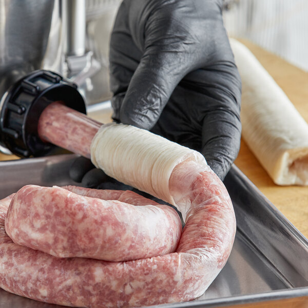 A person in a black glove wrapping Backyard Pro Butcher Series Collagen Sausage Casing around sausages on a tray.