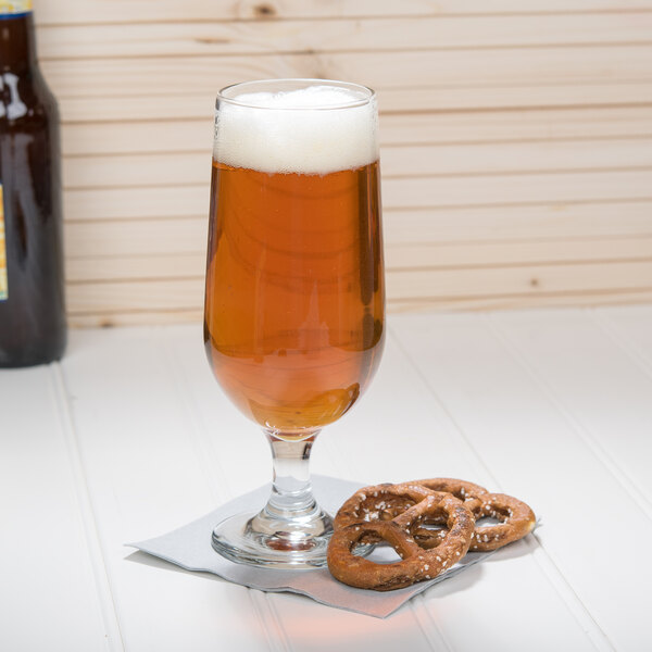 A Libbey stemmed pilsner glass of beer on a napkin with pretzels.