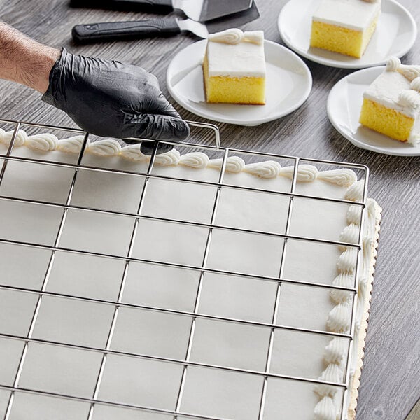 A person using a Choice stainless steel sheet cake marker to cut a cake.