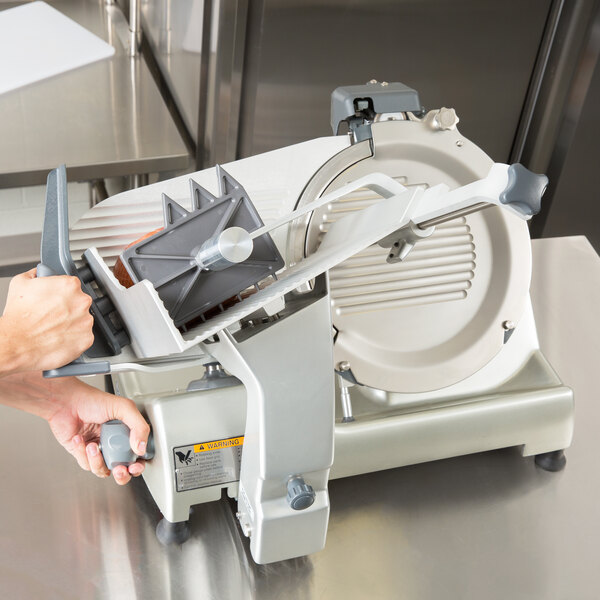 A person using a Hobart meat slicer to slice meat on a counter.