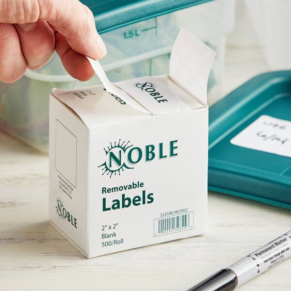 A person's hand opening a small white box of Noble Products removable blank labels.