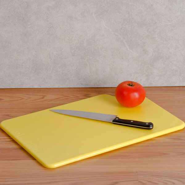 A yellow San Jamar cutting board with a knife on it cutting a tomato.