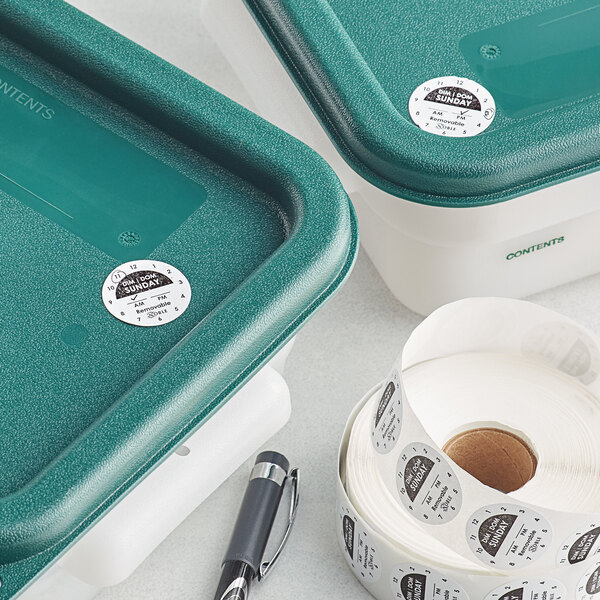 Two green containers with Noble Products Sunday labels and a roll of white day of the week labels on a counter.