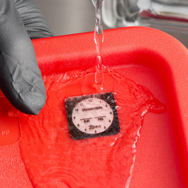A dissolvable clock label being rinsed with water in a red container.