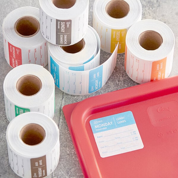 A table with several rolls of white paper labels and a red plastic container with white labels.