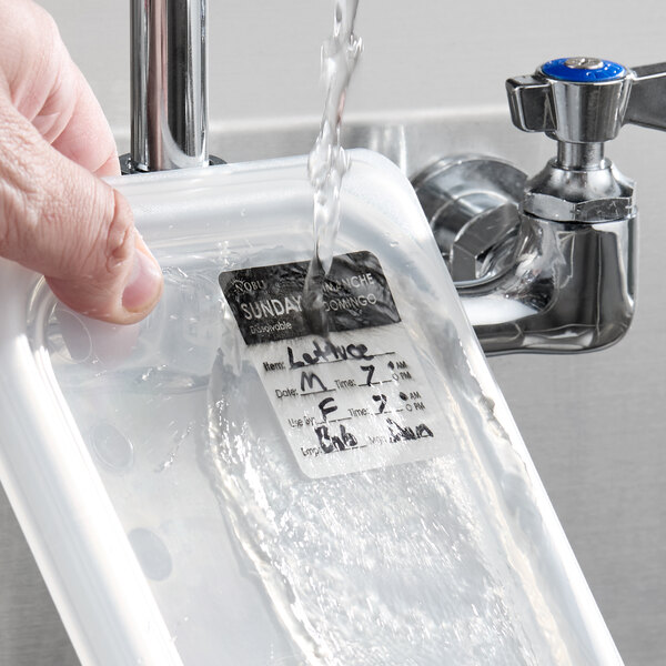 A dissolvable day of the week label being washed off a food container under running water.