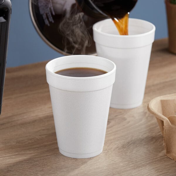 Two Dart white foam cups of coffee being poured on a counter.