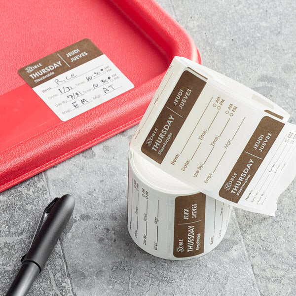 A red tray with a roll of Noble Products Thursday dissolvable day of the week labels and a pen on a counter.