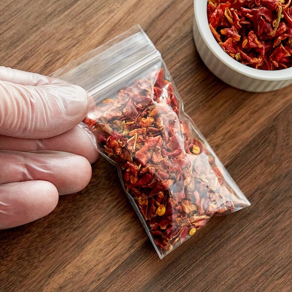 A hand holding a Clear Line plastic bag of dried red chili peppers.