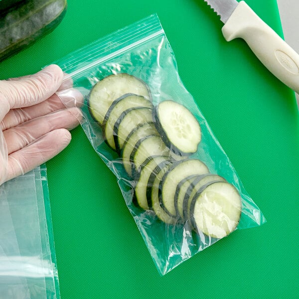 A gloved hand using a knife to slice cucumbers into a Clear Line plastic food bag.