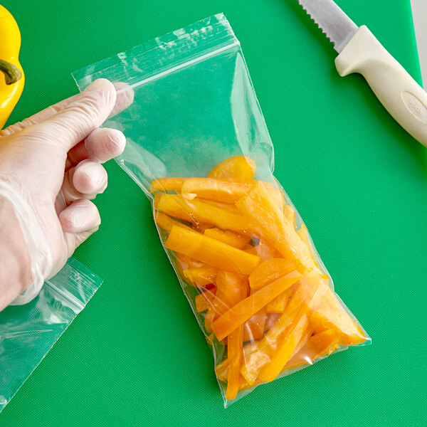 A hand in a glove sealing a Clear Line plastic bag of yellow peppers.