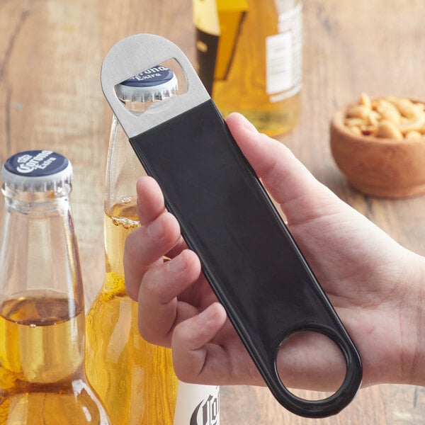 A hand using a Choice black bottle opener to open a glass bottle on a bar counter.