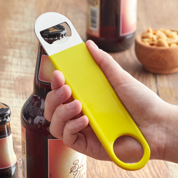A hand using a yellow Choice bottle opener to open a bottle.