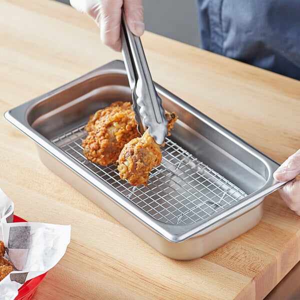 A person using tongs to serve food from a stainless steel tray on a metal rack.
