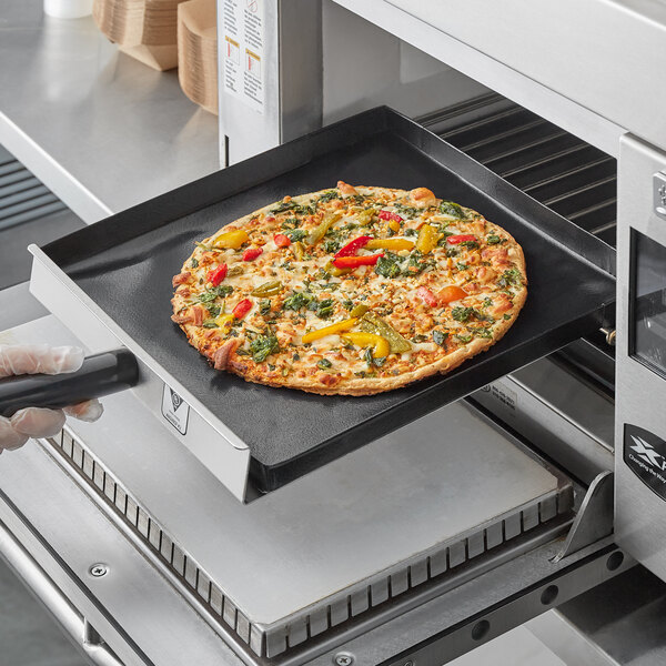 A Baker's Mark solid non-stick basket holding a pizza with vegetables being placed into a Rapid Cook oven.