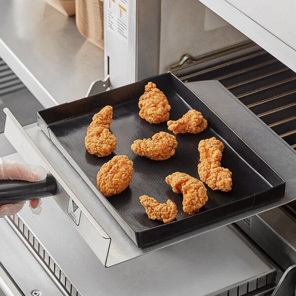 A hand holding a black Baker's Mark tray with fried chicken on it.