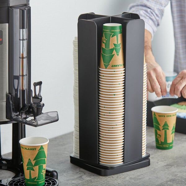 A man using a Choice Black revolving cup holder to fill a coffee cup with a white lid.