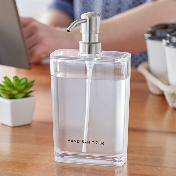 An American Metalcraft clear plastic rectangular hand sanitizer dispenser with liquid in it on a table.