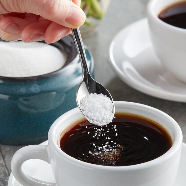 A hand holding a spoon with Splenda Monk Fruit Sweetener over a cup of coffee.