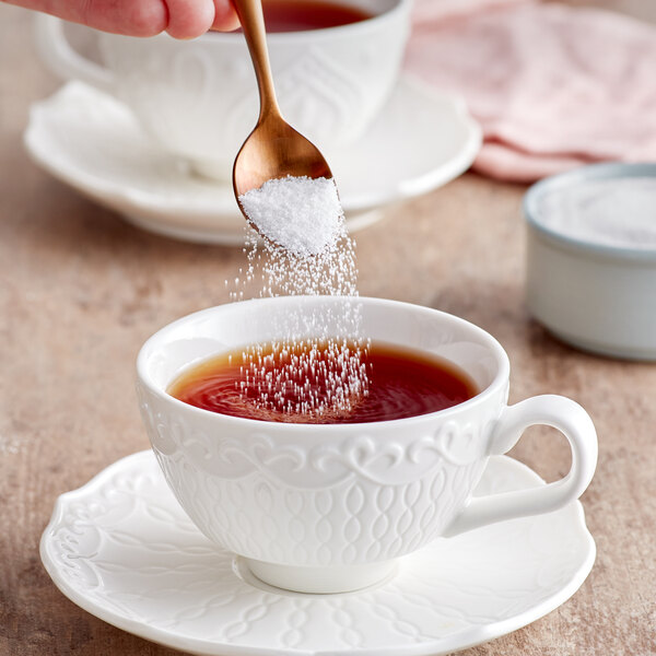 A hand pouring Splenda sugar blend into a cup of tea.