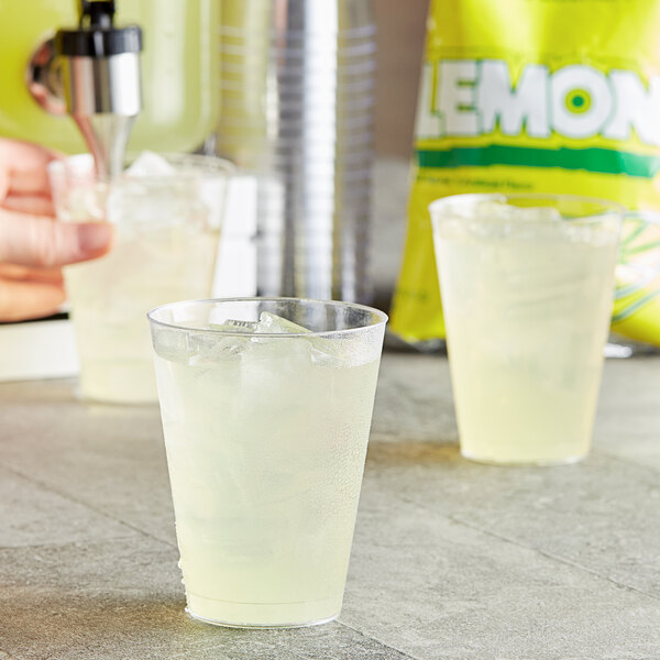 A hand pouring DominAde lemonade into a glass with ice.