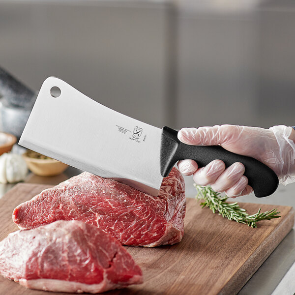 A hand in a plastic glove using a Mercer Culinary cleaver to cut a piece of meat.