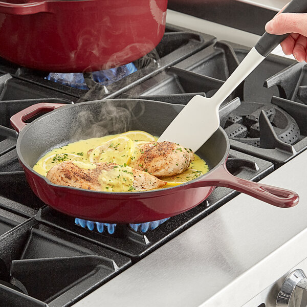 A person cooking food in a Valor Merlot enameled cast iron skillet on a stove top.