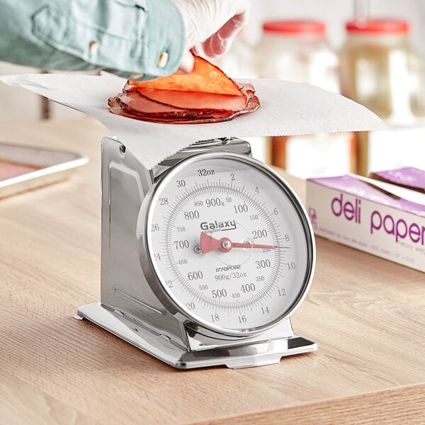 A person using a Galaxy mechanical portion scale to weigh food on a counter.