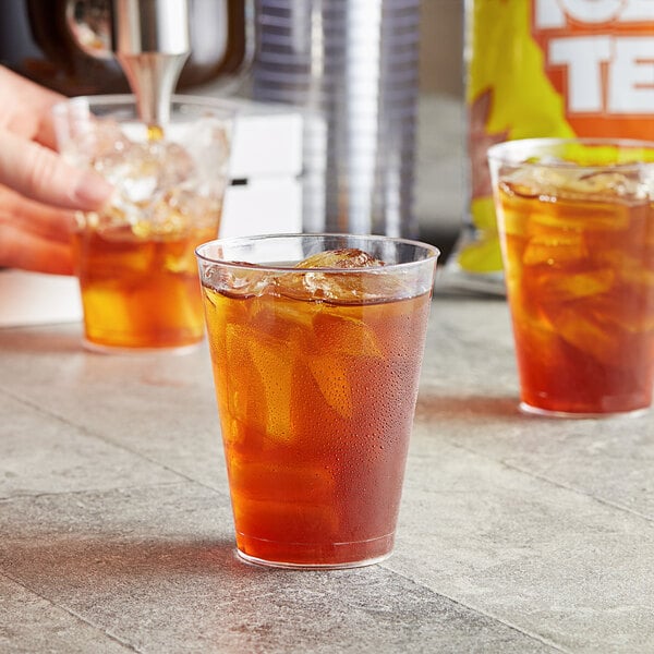 A hand pouring DominAde Iced Tea Drink Mix into a glass of ice tea.