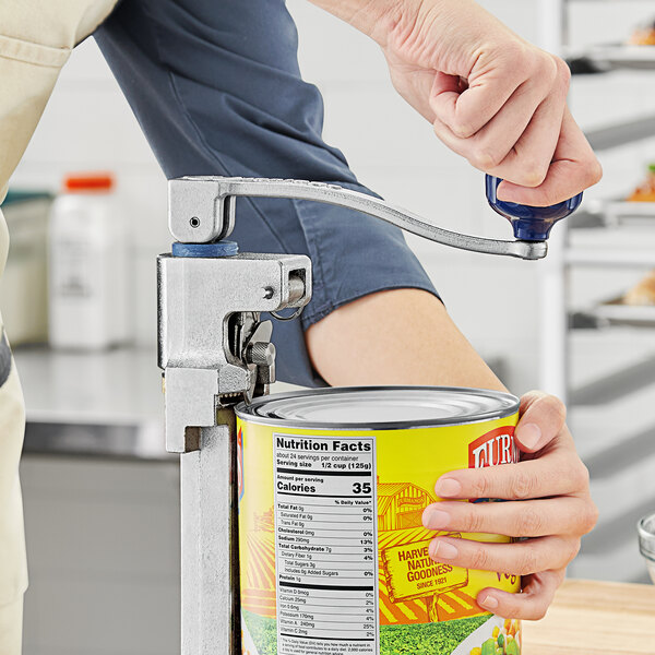 A person using an Edlund manual can opener to open a can of food on a counter in a professional kitchen.