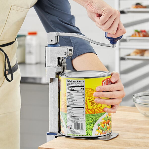 A person using an Edlund manual can opener to open a can of food.