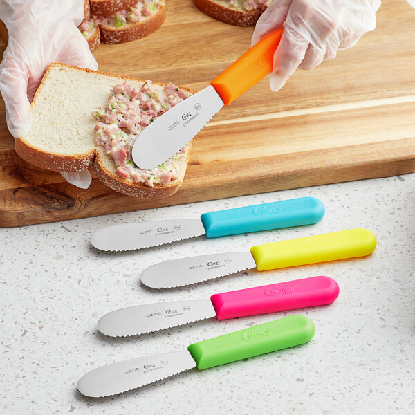 A person spreading food on a piece of bread with a Choice sandwich spreader with neon green handle.