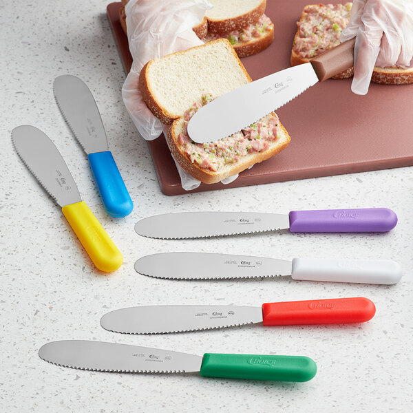 A person using a yellow Choice scalloped sandwich spreader to cut a sandwich.