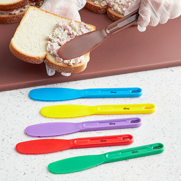 A hand using a green Choice sandwich spreader to spread spread on a sandwich.