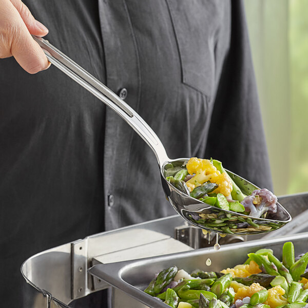 A person using a Vollrath stainless steel slotted oval serving spoon to serve food from a tray.