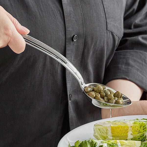 A person using a Vollrath stainless steel slotted oval serving spoon to serve food at a salad bar.