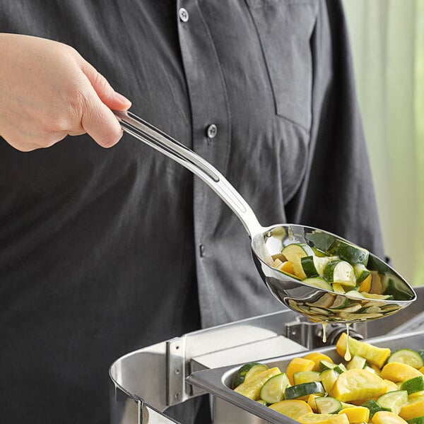 A person using a Vollrath stainless steel slotted serving spoon to serve food from a bowl.