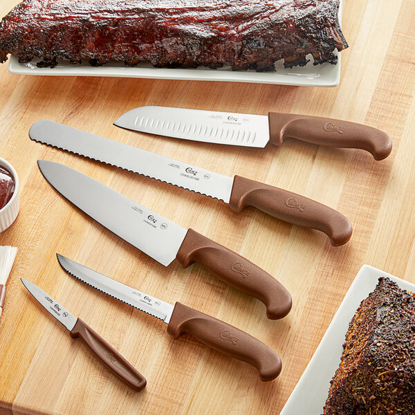 A Choice 5-piece knife set with brown handles on a table with a plate of ribs.