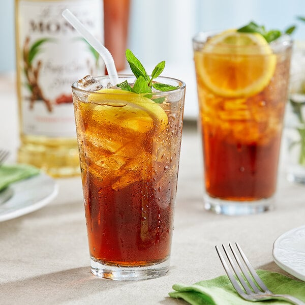 A glass of Monin pure cane iced tea with lemon slices and mint leaves with a straw.