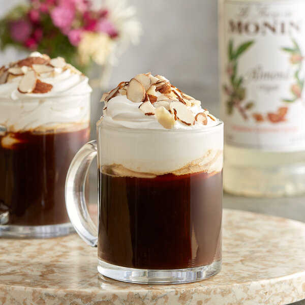 A glass mug of coffee with Monin Almond flavoring and whipped cream on top.