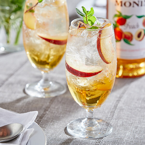 A glass of liquid with Monin Peach Flavoring, ice, and fruit.
