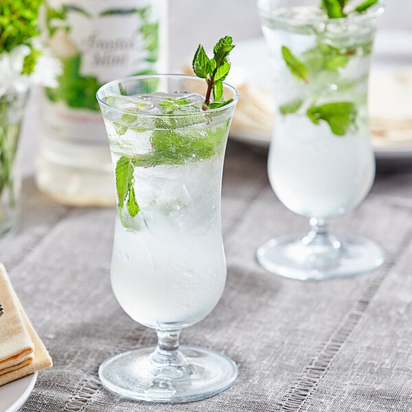 A glass of water with ice and Monin Premium Frosted Mint syrup with mint leaves.