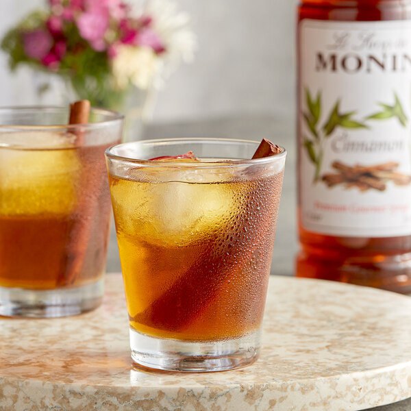 Two glasses of iced tea with Monin cinnamon flavoring syrup and cinnamon sticks on a table.