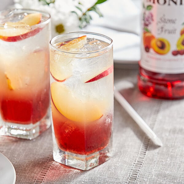Two glasses of fruit juice with Monin Premium Stone Fruit syrup on a table in a cocktail bar.