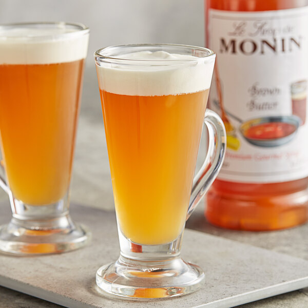 A bottle of Monin Premium Brown Butter flavoring syrup with a couple of glasses of liquid.