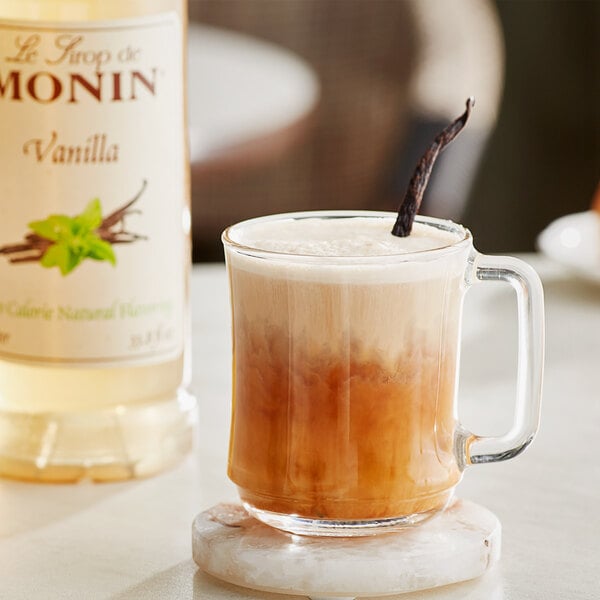 A glass mug of brown liquid with a Monin Natural Vanilla Flavoring Syrup stick in it.
