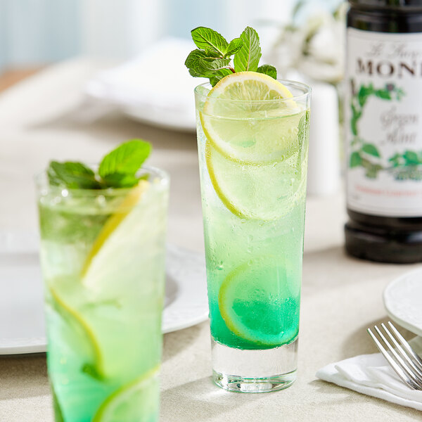 Two glasses of Monin green mint flavoring syrup with green liquid and lemon slices.