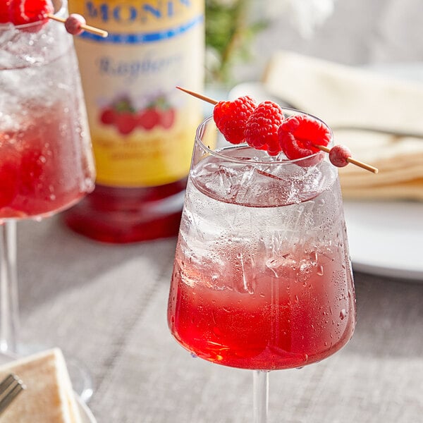A glass of Monin Sugar Free Raspberry fruit syrup and ice with a red liquid.