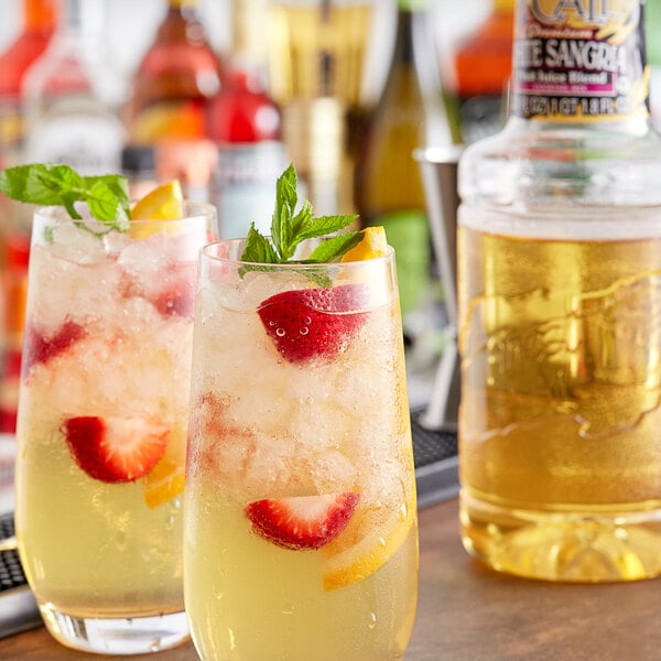 Two glasses of Finest Call White Sangria with ice and fruit on the side.
